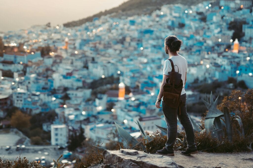 Traveler overlooking the blue city of Chefchaouen at dusk, Morocco, with hillside lights twinkling in the distance.