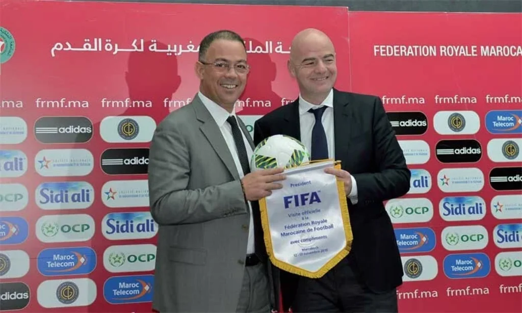 FIFA President Gianni Infantino and a Moroccan football official smiling and holding a FIFA pennant during a ceremony, highlighting Morocco’s rising influence in international football.