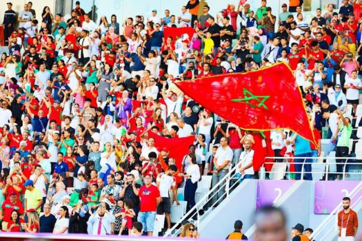 A crowd of Moroccan football fans waving flags and cheering in a stadium, symbolizing national pride before AFCON 2025