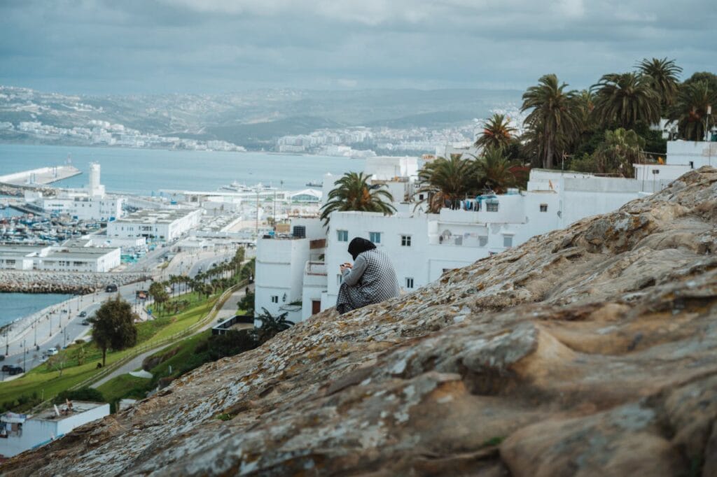 Woman sitting on a rocky slope overlooking Tangier’s white houses and the Mediterranean Sea