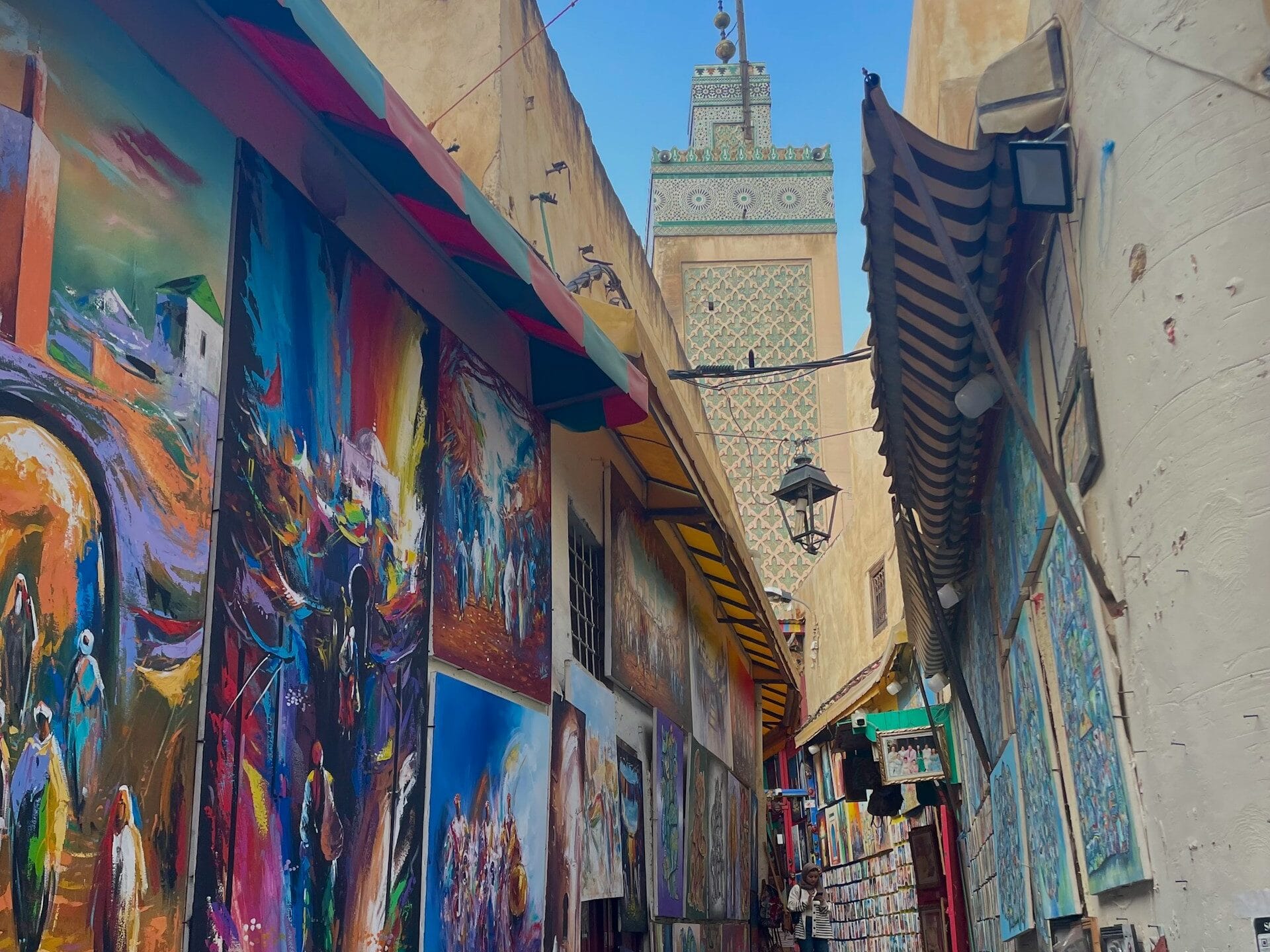 Colorful alley in Fez Medina lined with paintings and Moroccan art under a blue sky