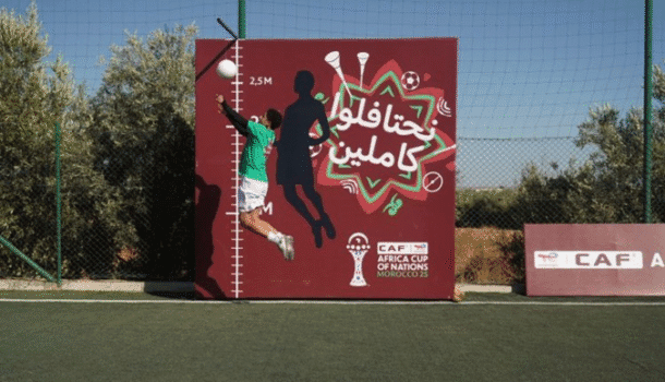 Young boy jumping to hit a football against an AFCON 2025 caravan activity board in Berkane, Morocco.