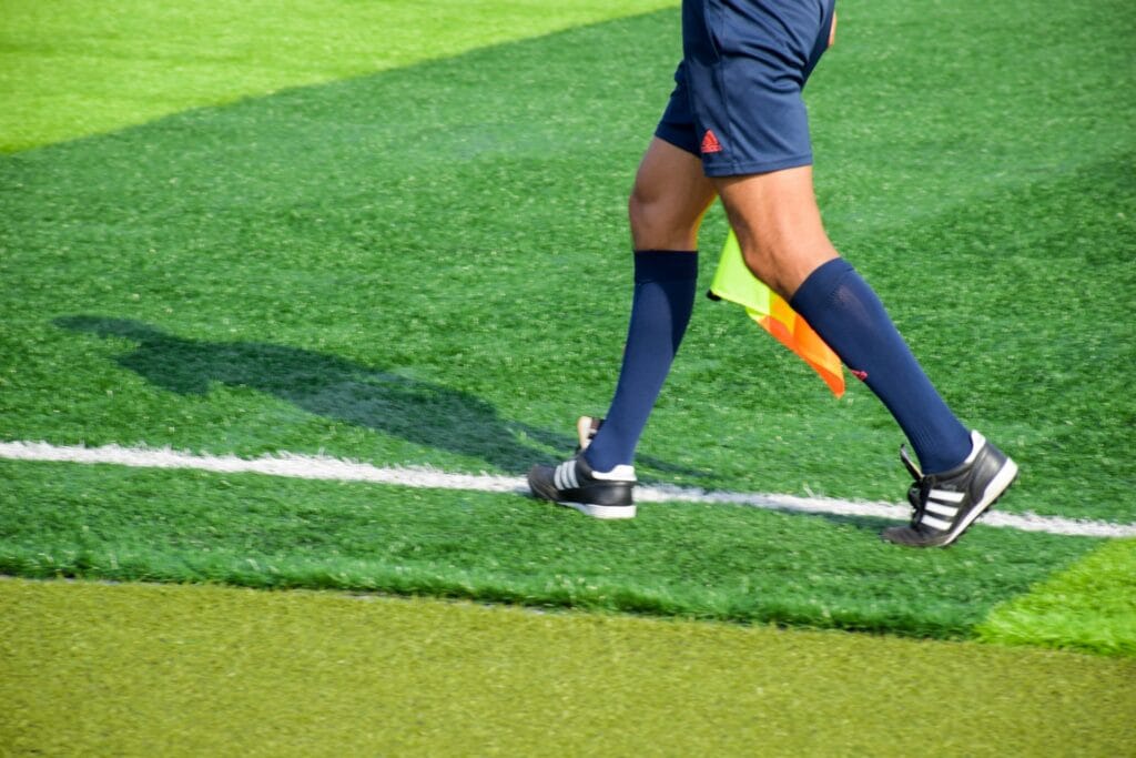 Assistant referee running along the touchline with a flag during a football match, symbolizing CAF match officials for AFCON 2025 in Morocco.