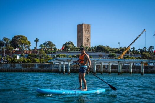 Man paddleboarding on the Bouregreg River in Rabat with the Hassan Tower in the background