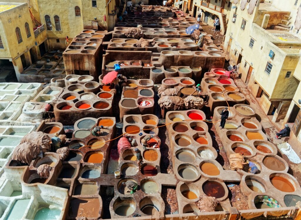 Aerial view of the Chouara Tanneries in Fez, Morocco, showing artisans working in traditional stone dye pits filled with colorful natural pigments inside the historic Medina.