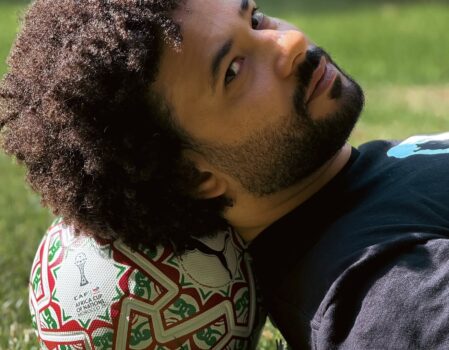 A man lying on the grass with his head resting on the AFCON 2025 ITRI match ball featuring Moroccan zellij patterns.