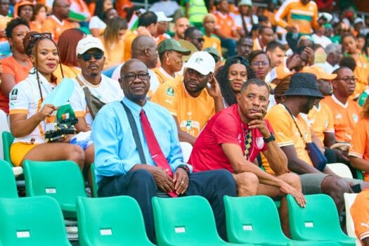 Ivorian football fans in orange jerseys supporting their national team in the stadium during an AFCON match.