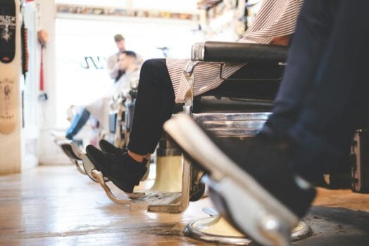 A man sitting in a barber chair at a modern barbershop, representing a viral story about a British traveler flying to Morocco for a haircut.