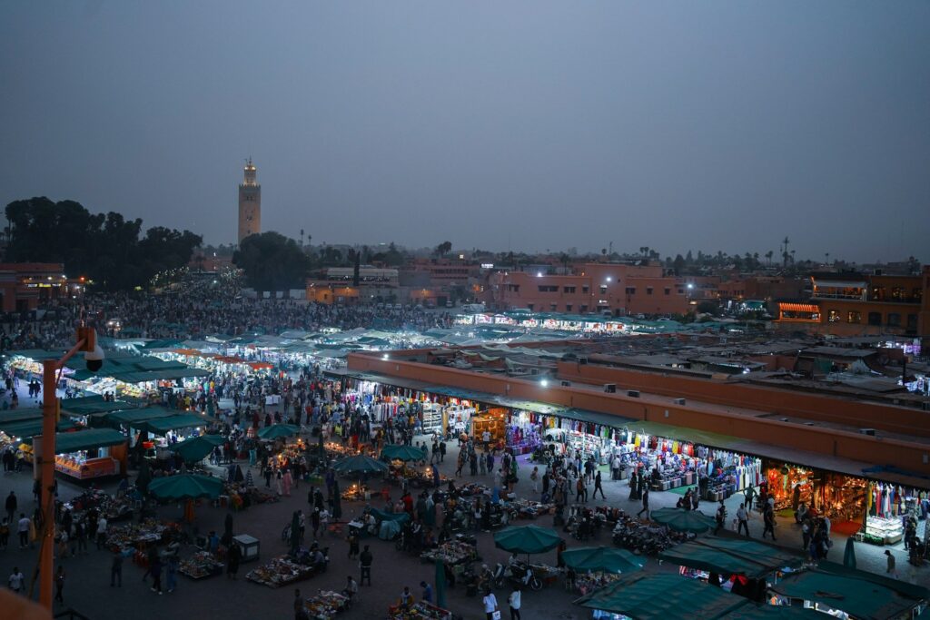 Night view of Jemaa el-Fna in Marrakech with market stalls, crowds and the Koutoubia Mosque rising in the background.