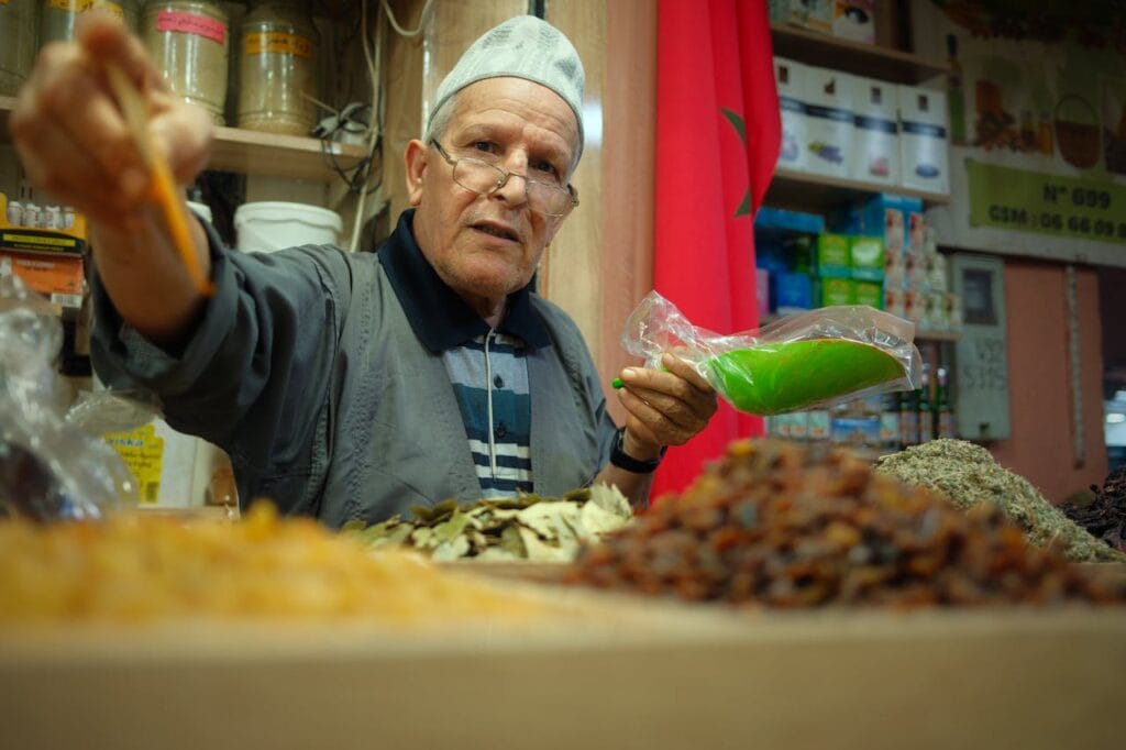 A Moroccan spice merchant holding herbs and powdered spices inside a traditional souk.