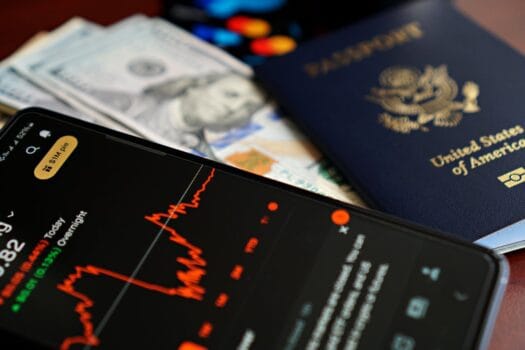 A close-up of a smartphone showing financial data beside a U.S. passport and dollars, representing digital travel trends and data-driven tourism.