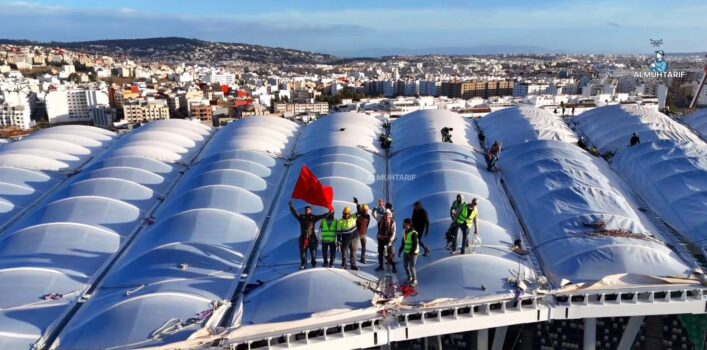 Workers standing on the newly completed roof of the Grand Stade de Tanger holding the Moroccan flag