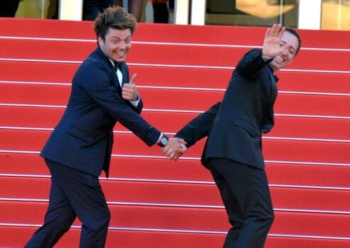 Comedians waving and smiling on a red carpet during a film festival appearance