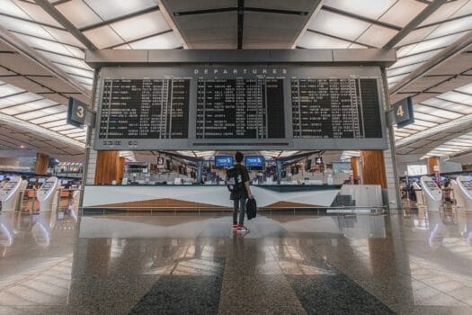 Traveler checking departure board inside a modern airport terminal during global flight schedule disruptions.