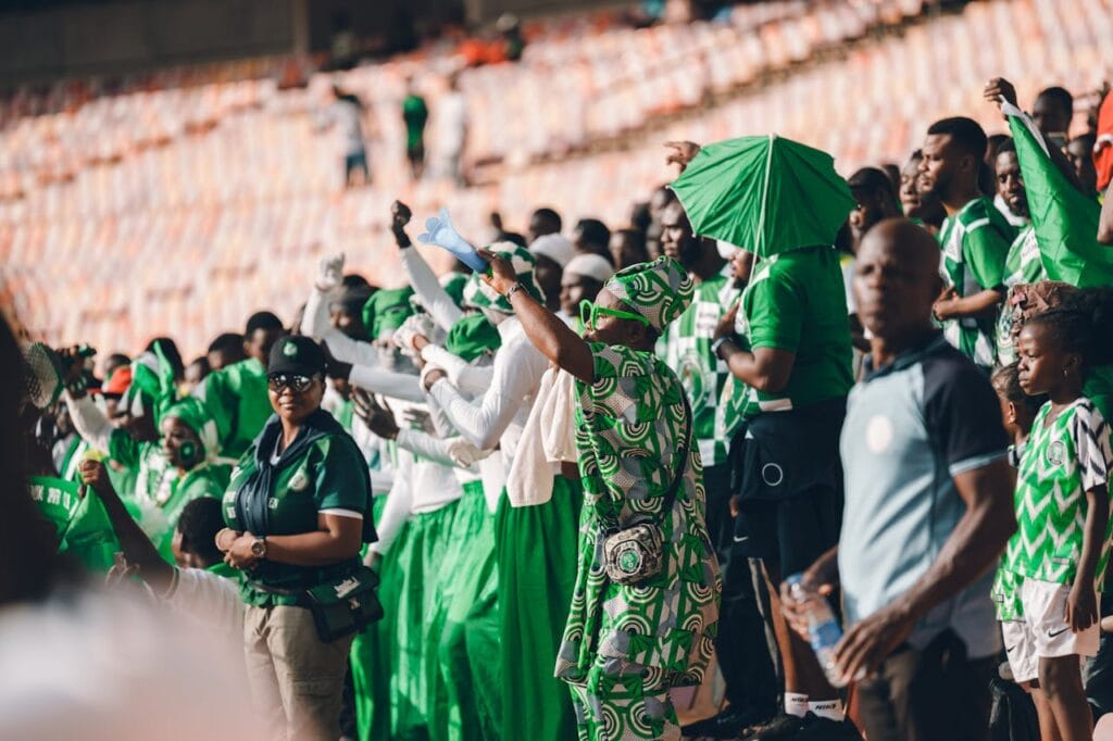 Nigerian football fans dressed in green cheering passionately in the stands during a match, symbolizing support for the Super Eagles ahead of AFCON 2025.