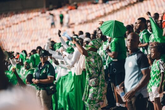 Nigerian football fans dressed in green cheering passionately in the stands during a match, symbolizing support for the Super Eagles ahead of AFCON 2025.