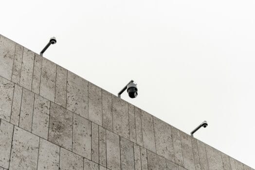 Three surveillance cameras installed on the edge of a modern building, symbolizing urban monitoring infrastructure.