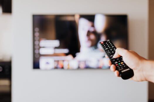 Person holding a TV remote while browsing a streaming platform on a smart TV screen.