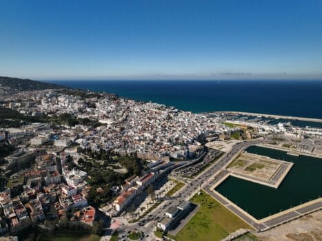 Aerial view of Tangier showing the cityscape, marina, and Mediterranean coastline under clear blue skies.