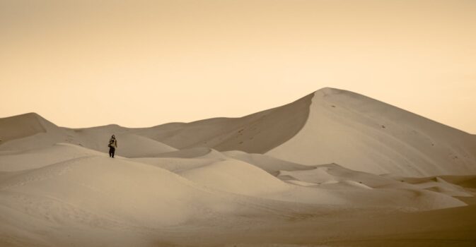 A lone traveler walking across pale sand dunes at dawn in the Merzouga desert, Morocco